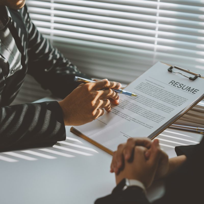 Employer reviewing a candidate's resume in a bright, modern office, highlighting qualifications whil